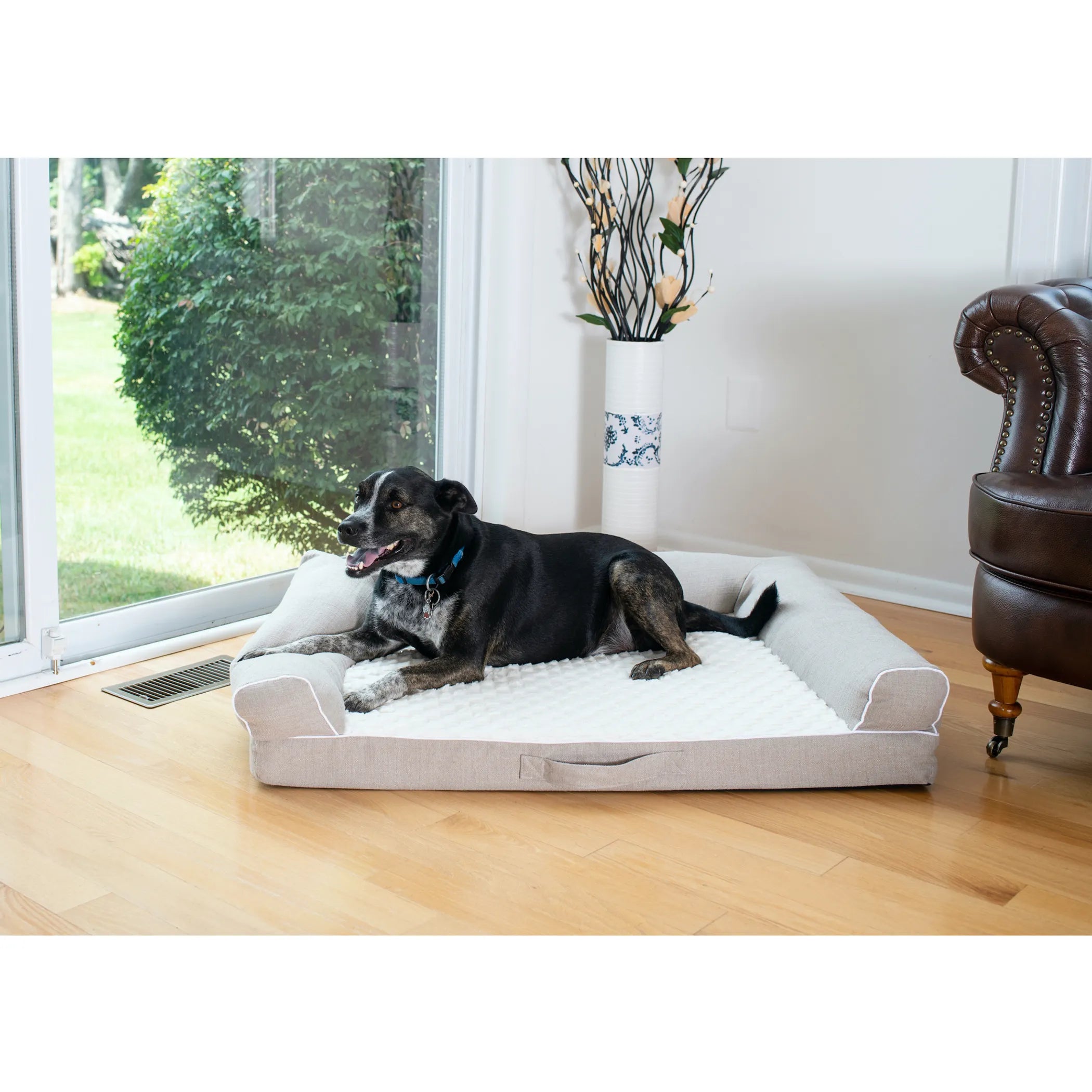 Dog lying on a large orthopedic pet bed in a room with wooden flooring 