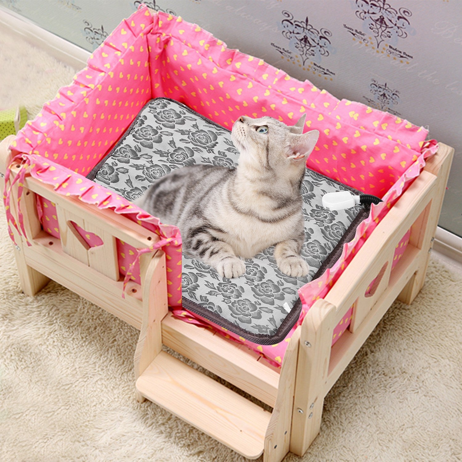 Cat lying on a heating pad in a wooden pet bed with pink bedding